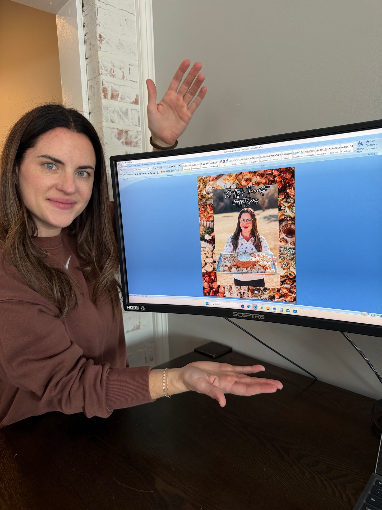 Sarah Kraffty standing next to a computer monitor showing the digital version of the "Kraffty's Favorite Appetizers" book.